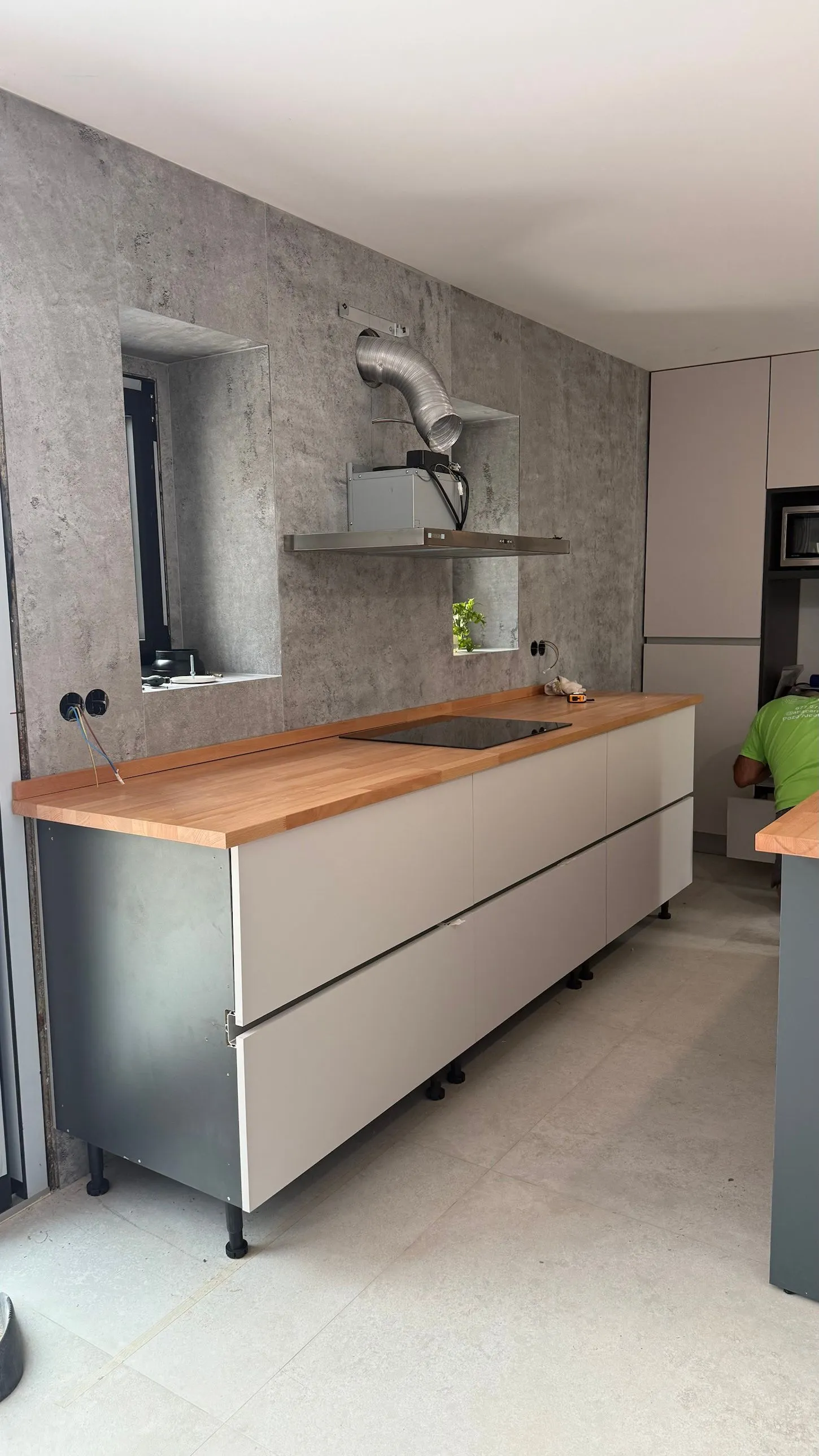 Cocina con muebles blancos sin tirador, encimera de haya maciza y pared revestida con Kobert In efecto cemento