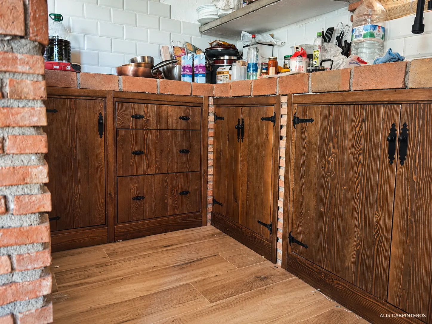 Cocina rústica con frentes de madera de pino teñida, herrajes de forja y encimera de ladrillo