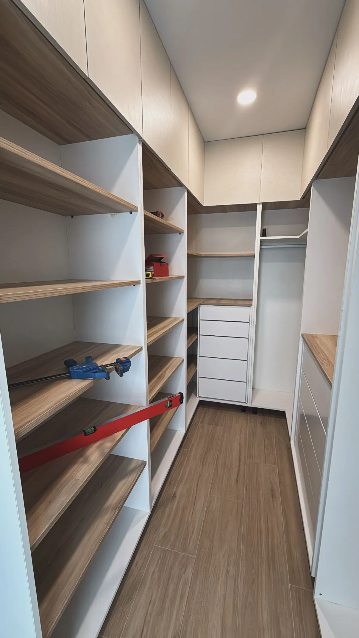 Vestidor en forma de U con baldas en acabado madera, cajoneras blancas y altillos